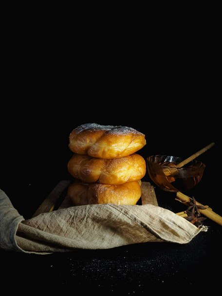 Свежая булочка с корицей или сладкая булочка с медом изолированы в деревенском темном фоне с избирательным фокусом и копирования пространства. Кондитер. Фотография тёмной еды. - Фото, изображение