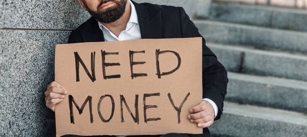 Αγνώριστος ώριμος επιχειρηματίας κρατώντας αφίσα χαρτόνι με Need Money κείμενο, πανόραμα, καλλιέργεια - Φωτογραφία, εικόνα