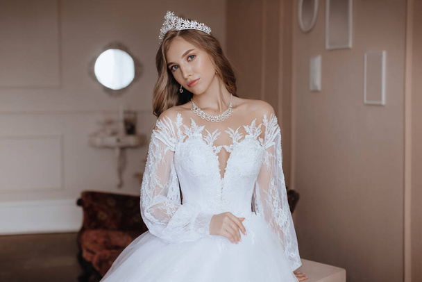Beautiful young bride with light make-up in white dress  in an exquisite interior  - Фото, зображення