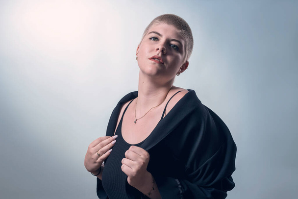 studio shot of a young, strong woman with very short blond hair in black clothes - Fotó, kép