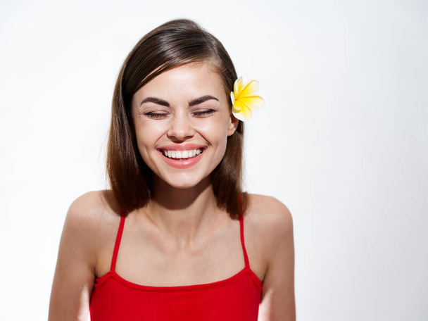 σέξι μελαχρινή χαμογελά σε ένα ελαφρύ φόντο και ένα κίτρινο λουλούδι στα μαλλιά της - Φωτογραφία, εικόνα