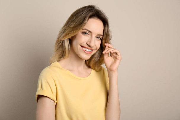 Portrait of happy young woman with beautiful blonde hair and charming smile on beige background - 写真・画像
