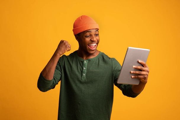 Sukces online. Wesoły Afroamerykanin z cyfrowym tabletem świętuje sukces - Zdjęcie, obraz