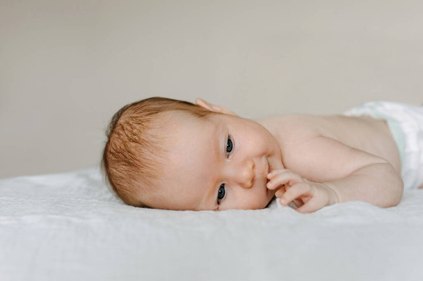 Newborn baby smiling, lying on bed on tummy. - Foto, afbeelding