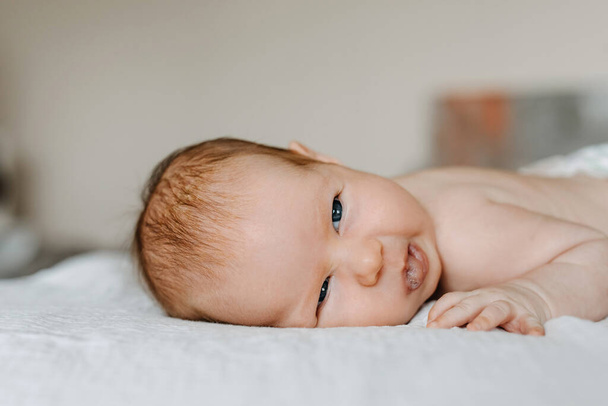 Pasgeboren baby maakt grappig gezicht, glimlacht, ligt op bed. - Foto, afbeelding