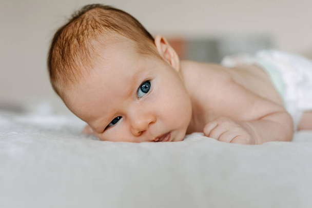 Bambino di due mesi che fa la faccia concentrata seria, sdraiato sul letto. - Foto, immagini