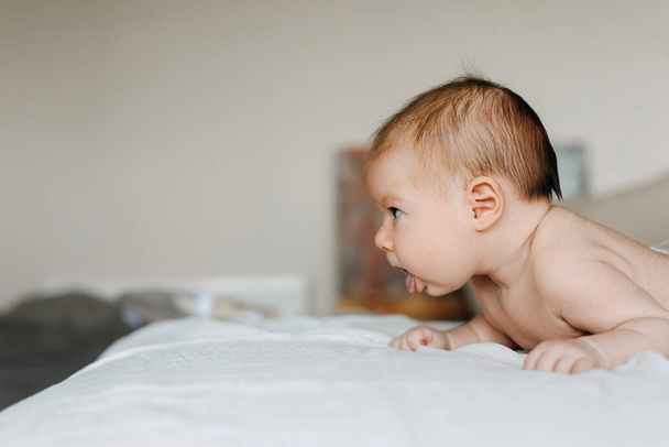 Due mesi bambino tenendo la testa in su, mostrando la lingua. - Foto, immagini