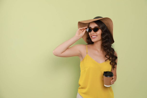 Beautiful young woman with straw hat and cup of coffee on light green background. Space for text - Valokuva, kuva