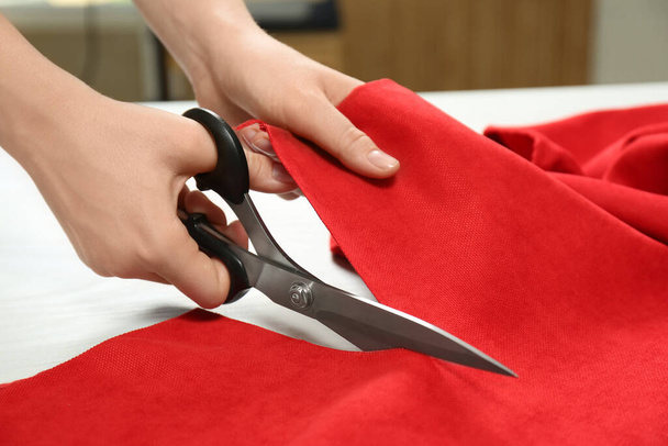 Seamstress cutting red fabric with scissors at workplace, closeup - Foto, imagen