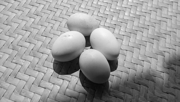 Фотографія 4 курячих яєць на чорно-білій темі на тлі тканого бамбука
 - Фото, зображення