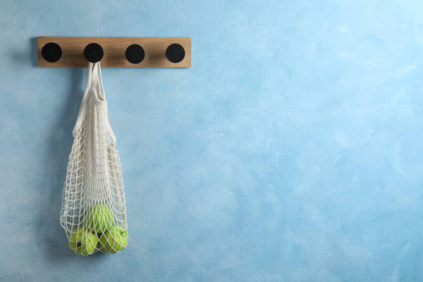 Support en bois avec de délicieuses pommes dans un sac en maille sur un mur bleu clair. Espace pour le texte - Photo, image