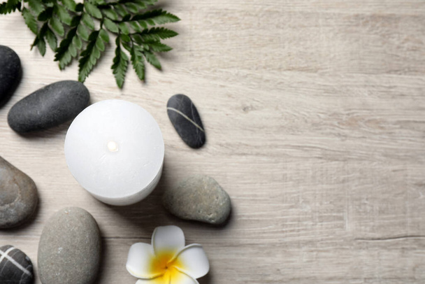 Burning candle, plumeria flower and spa stones on light beige wooden table, flat lay. Space for text - Foto, Imagem