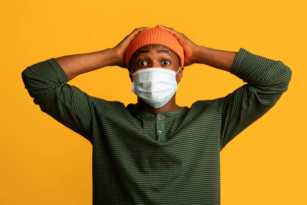 Πανικός του Coronavirus. Φοβισμένος Αφροαμερικανός με την ιατρική μάσκα που ακουμπάει το κεφάλι με σοκ - Φωτογραφία, εικόνα