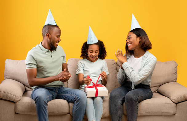 Nadšení afroameričtí rodiče dělají překvapení pro svou krásnou dceru, dávají dárek box, pozdrav s narozeninami - Fotografie, Obrázek