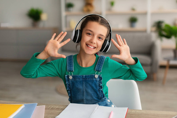 Chica sentada en el escritorio, agitando las manos con auriculares - Foto, imagen