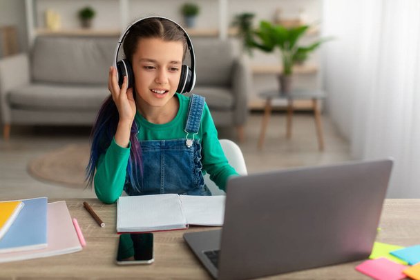 Dziewczyna siedząca przy stole, używająca laptopa, nosząca dotykowe słuchawki - Zdjęcie, obraz