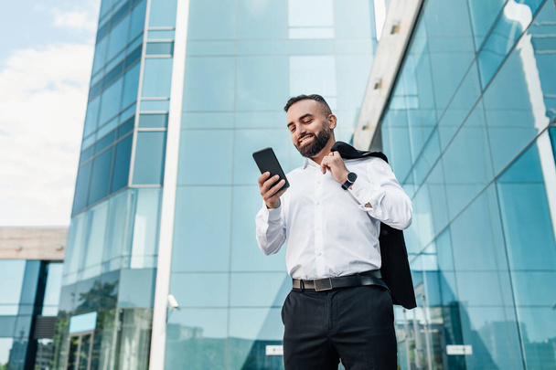 Obchodní životní styl. Starší podnikatel s chytrým telefonem v ruce chatování s klientem, stojí proti kancelářské centrum - Fotografie, Obrázek