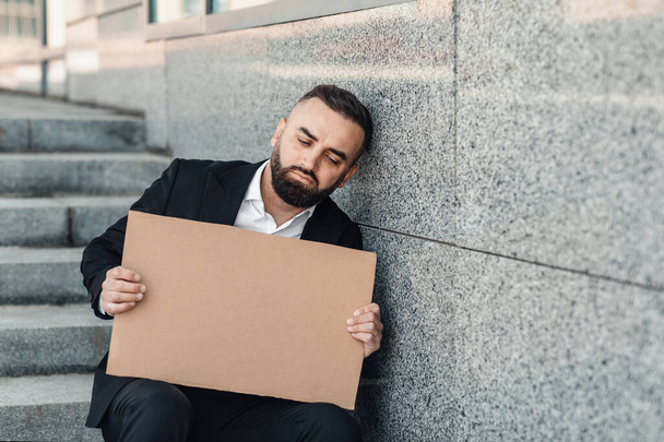 Беспокойный офисный работник держит пустой картон, сидя на улице на лестнице, свободное место - Фото, изображение