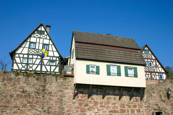 vieille maison construite au-dessus des remparts médiévaux à côté de deux maisons à colombages à Hirschhorn dans le sud de l'Allemagne avec drapeau local accroché par une fenêtre - Photo, image
