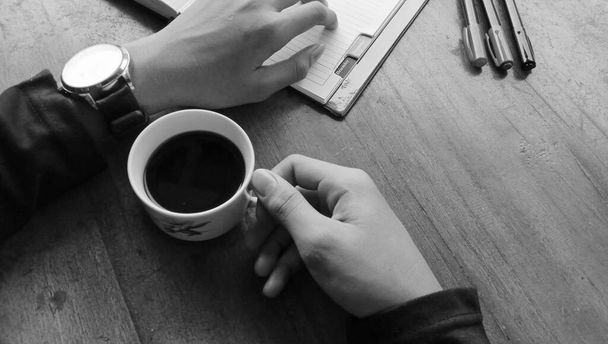 Fotografie osoby těší šálek černé kávy na dřevěném stole - Fotografie, Obrázek