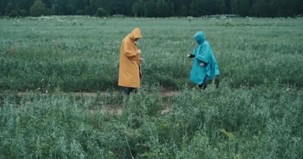 Mann in gelbem Regenmantel und Frau in blauem Regenmantel tanzen eine Drehung in einem Feld - Filmmaterial, Video