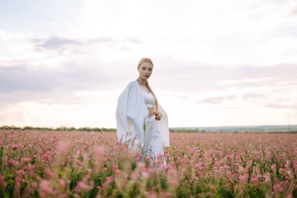 Beauty romantic girl Outdoors at sunset. Young woman in stylish clothes posing in the blooming field. Nature, vacation, relax and lifestyle. Fashion concept. - Foto, Imagem