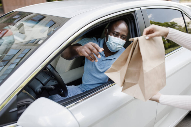 Black guy driver in face mask taking take away food - Фото, зображення