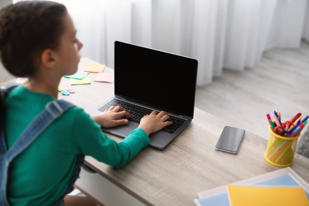 Mädchen sitzt am Schreibtisch, benutzt leeren Laptop, tippt auf der Tastatur - Foto, Bild
