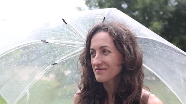 Ragazza sorridente sotto l'ombrello, video al rallentatore, donna senza trucco sotto l'ombrello trasparente durante la pioggia estiva - Filmati, video