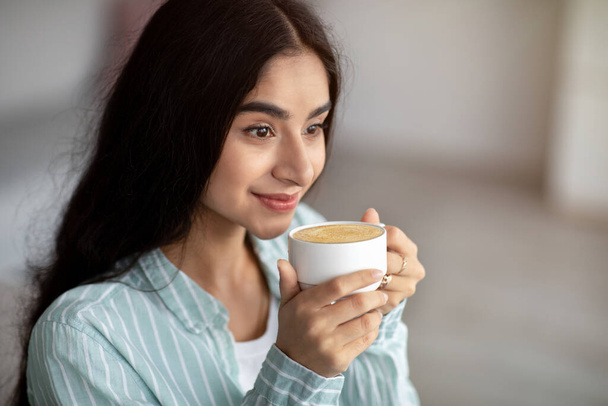 Jonge Indiase vrouw met koffiepauze, drinken schuimige cappuccino thuis, kopieerruimte - Foto, afbeelding