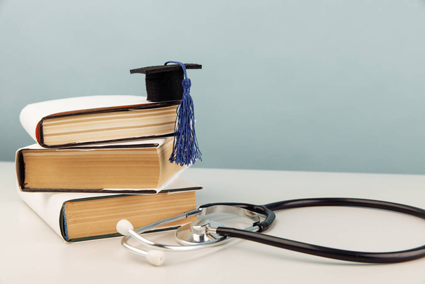 Orvosi oktatás koncepciója. Stethoscope és érettségi sapka egy halom könyvet a kék háttér - Fotó, kép