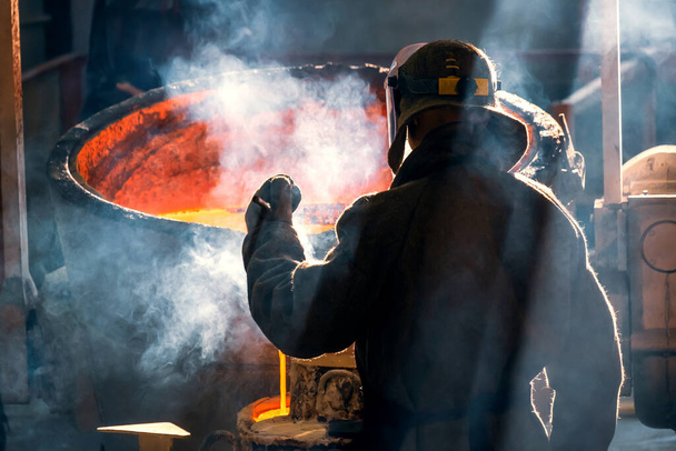 εργάτης χυτηρίου μετάλλων και κραμάτων σε μεταλλουργική μονάδα, οπίσθια όψη. καπνός από κόκκινο μέταλλο - Φωτογραφία, εικόνα