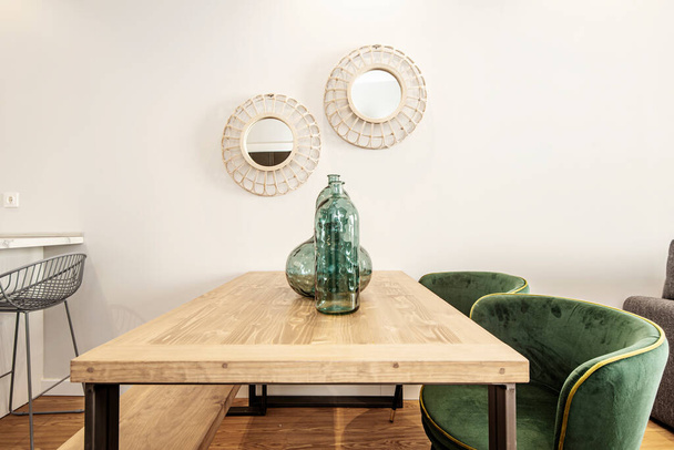 Table en bois veiné, miroirs sur le mur, grands vases et chaises de tapisserie en velours vert. Salle à manger dans un appartement de location de vacances - Photo, image