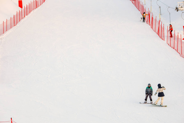 two snowboarders on the ski slope talking while standing on snowboards. the track is fenced with a red mesh fence - Photo, Image
