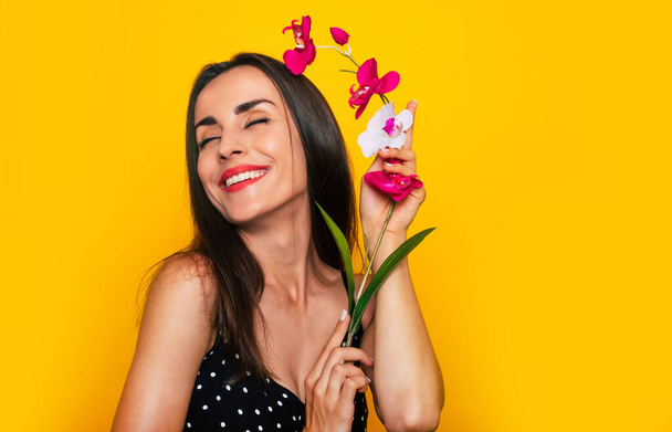 Gorgeous tender smiling woman is posing with a flower in hands isolated on yellow background - Fotografie, Obrázek