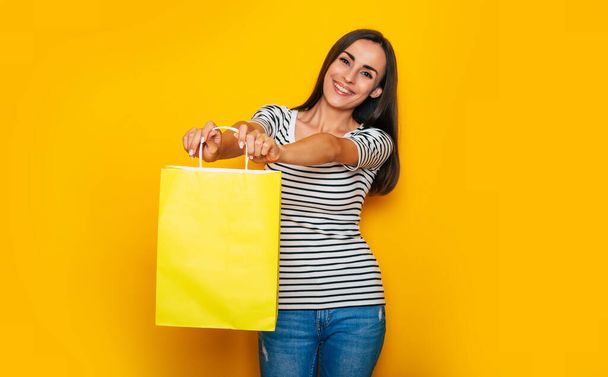 Beautiful happy excited brunette woman in casual clothes is posing with shopping bags isolated on yellow background - Foto, imagen