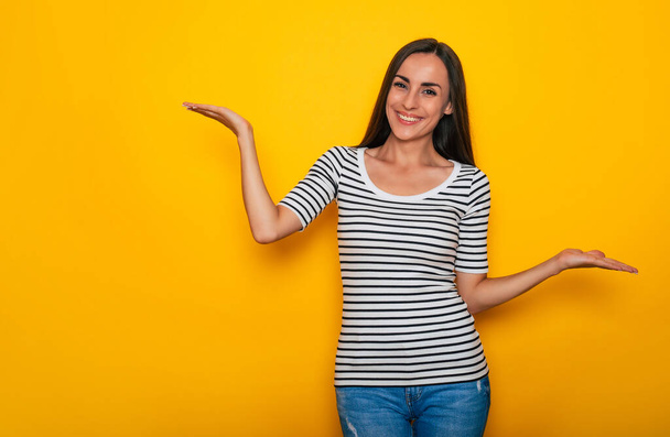 Beautiful smiling modern brunette woman in casual wear is posing against yellow wall - 写真・画像
