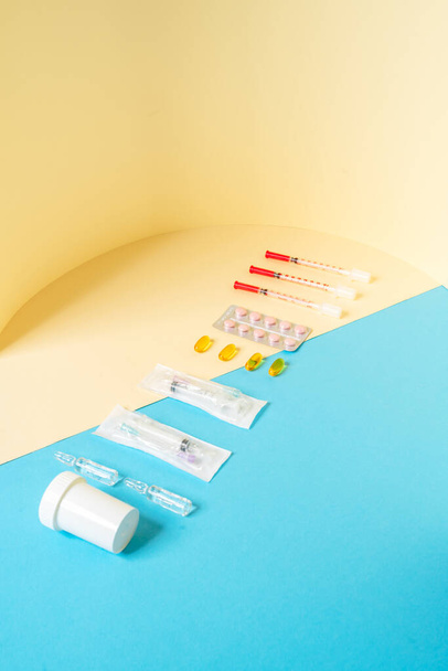 The set of a medical devices consisting of syringes, jar, tablets, ampoules standing on the beige and blue background in the studio - Foto, afbeelding