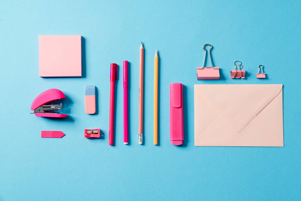 Overhead view of a set for writing consisting of: letter, marker, pen, pencil, eraser, stapler, paper lying in a blue studio - Фото, изображение