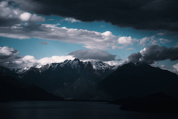 A landscape of a lake surrounded by rocky mountains covered in the snow under a dark cloudy sky - Foto, immagini