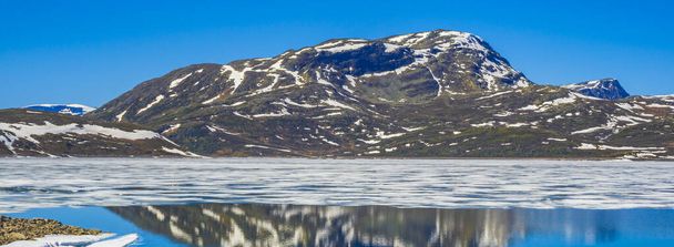 Frozen turquoise lake Vavatn panorama in summer landscape and mountains with snow in Hemsedal Norway. - Foto, imagen