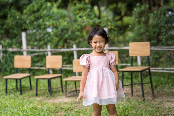 A cheerful little Asian girl against wooden chairs outdoors - Photo, image