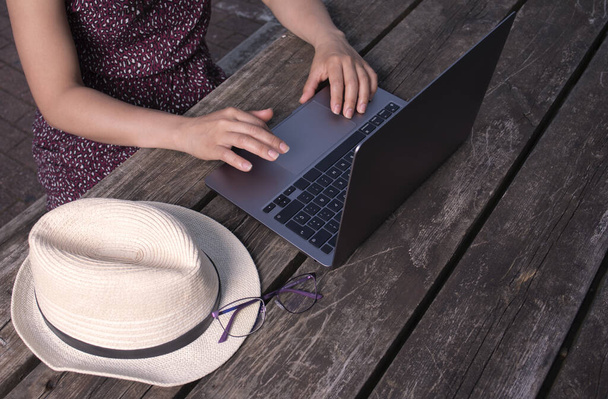 A closeup of a woman working on her laptop outdoors on a wooden desk, during daylight - Fotoğraf, Görsel