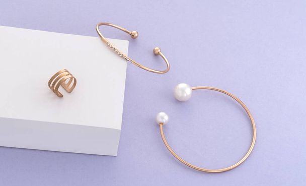 Modern arany karkötők és gyűrű fehér doboz lila háttér - Fotó, kép