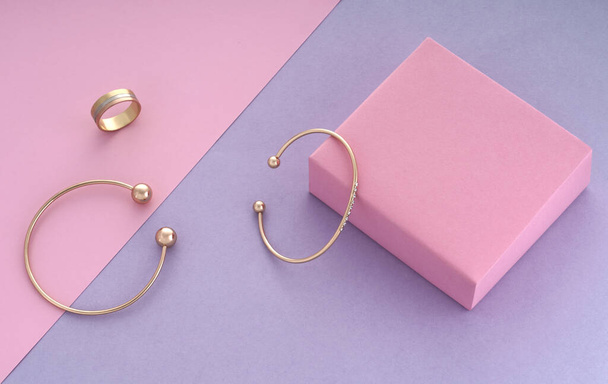 Zwei moderne Armbänder und dreifacher Ring auf rosa und lila Hintergrund mit Kopierraum - Foto, Bild