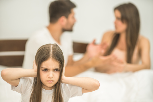 L'infelice ragazza seduta vicino ai genitori litiganti sul letto
 - Foto, immagini