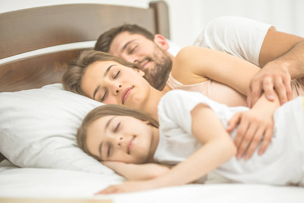 Η κόρη και οι γονείς κοιμούνται στο κρεβάτι. - Φωτογραφία, εικόνα