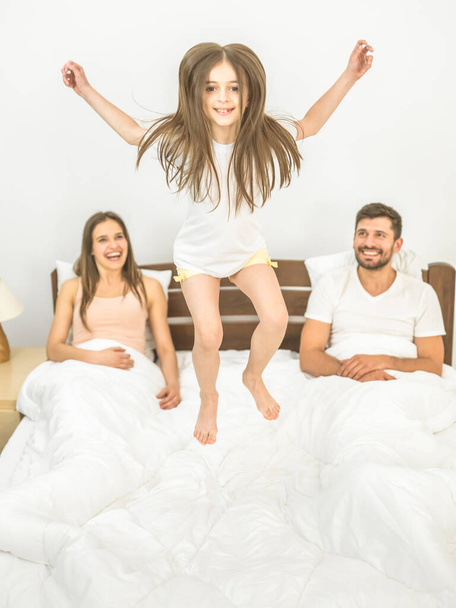 Το κορίτσι που πηδάει στο κρεβάτι κοντά στους γονείς. - Φωτογραφία, εικόνα