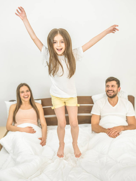 Das Mädchen springt in der Nähe der Eltern auf das Bett - Foto, Bild