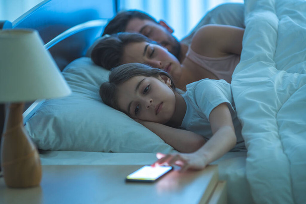 La petite fille téléphone près des parents endormis. nuit - Photo, image